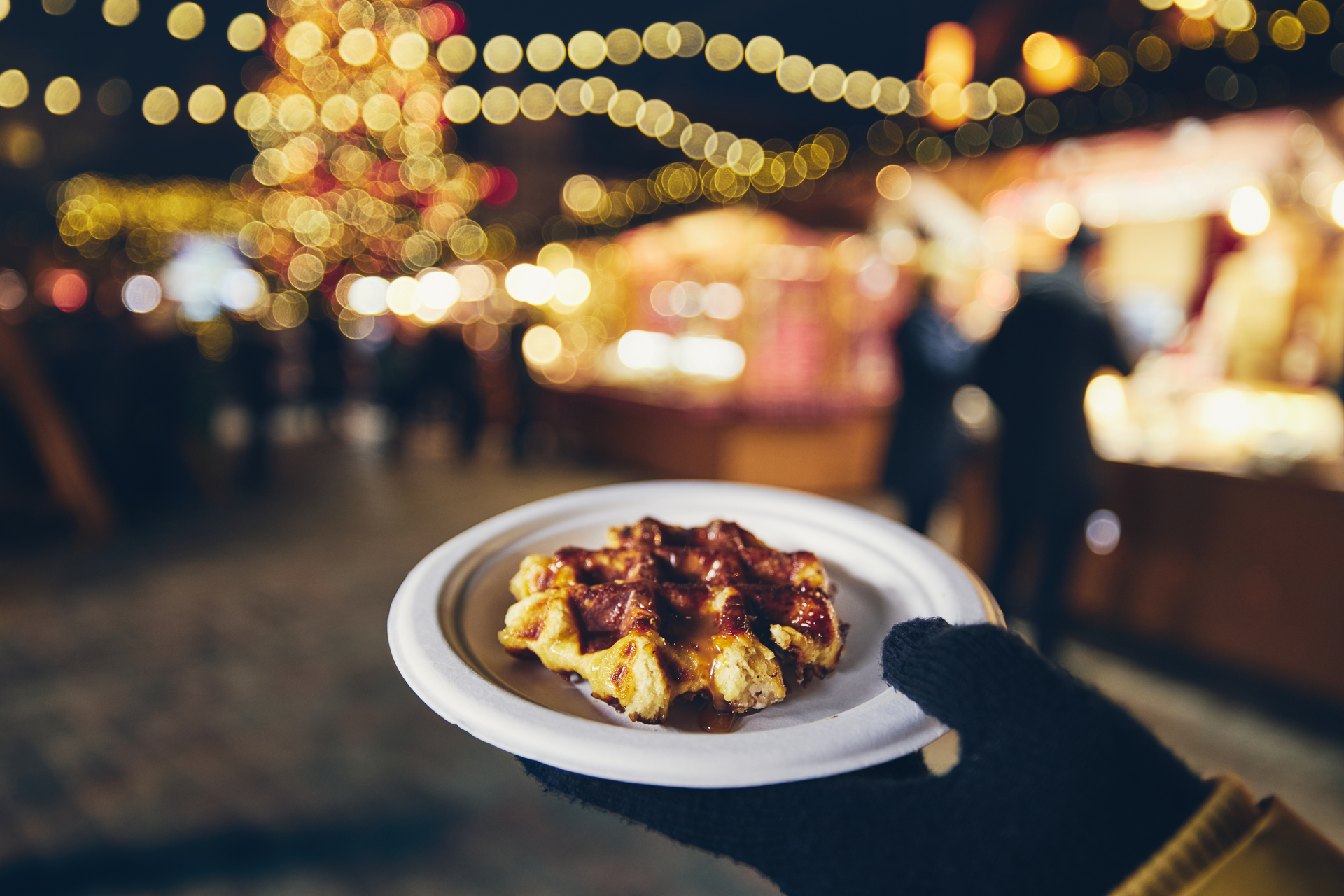 Gaufre tenue devant les lumières d’un marché de Noël